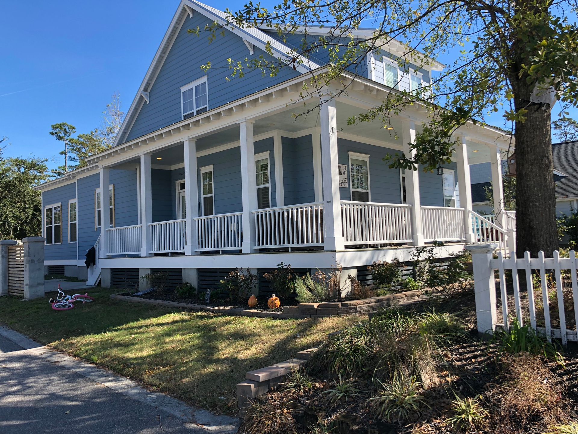 Blue house with white porch, railing, and trim; small front yard with picket fence.