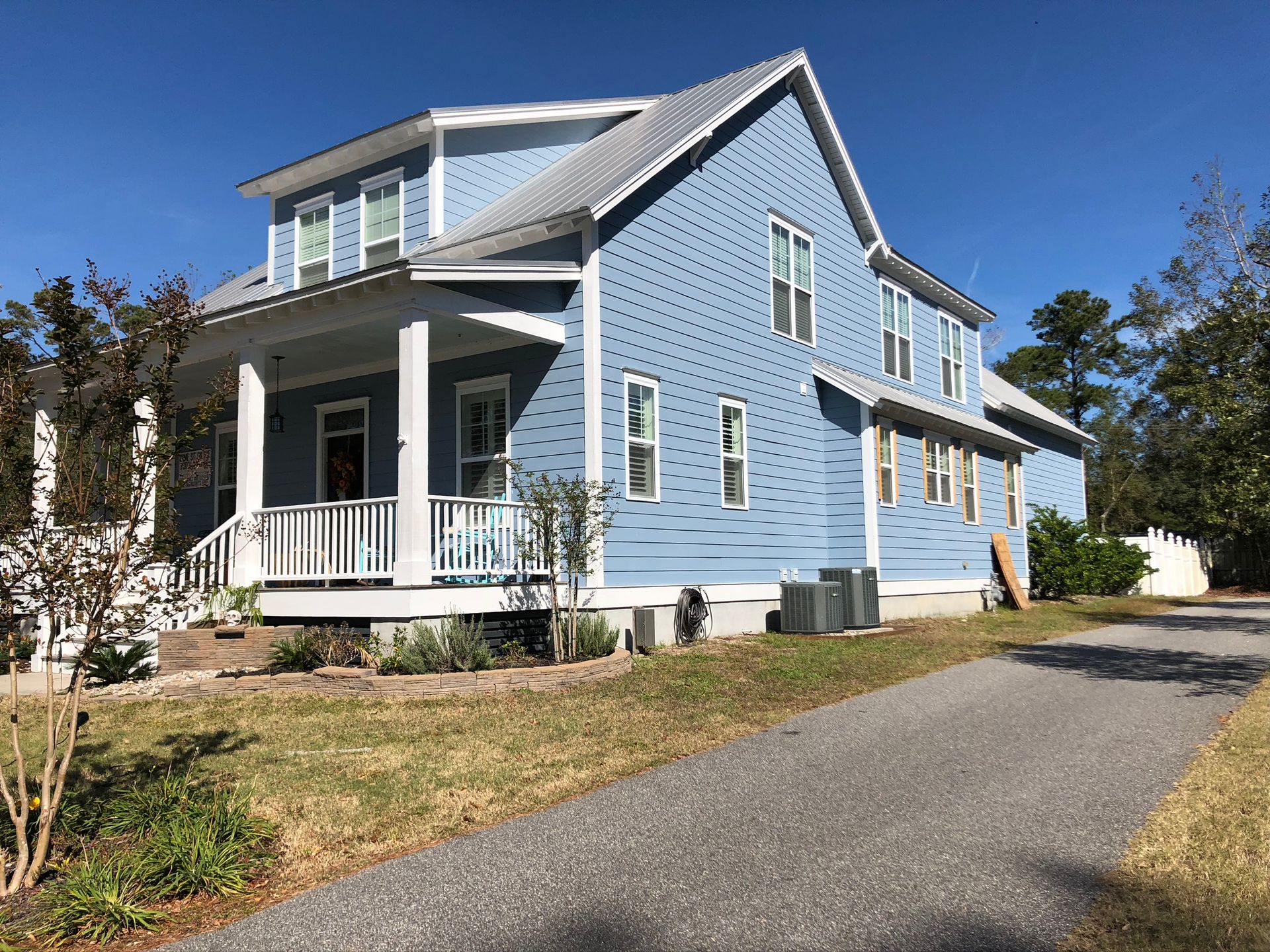 Light blue two-story house with a porch and gray metal roof on a sunny day.