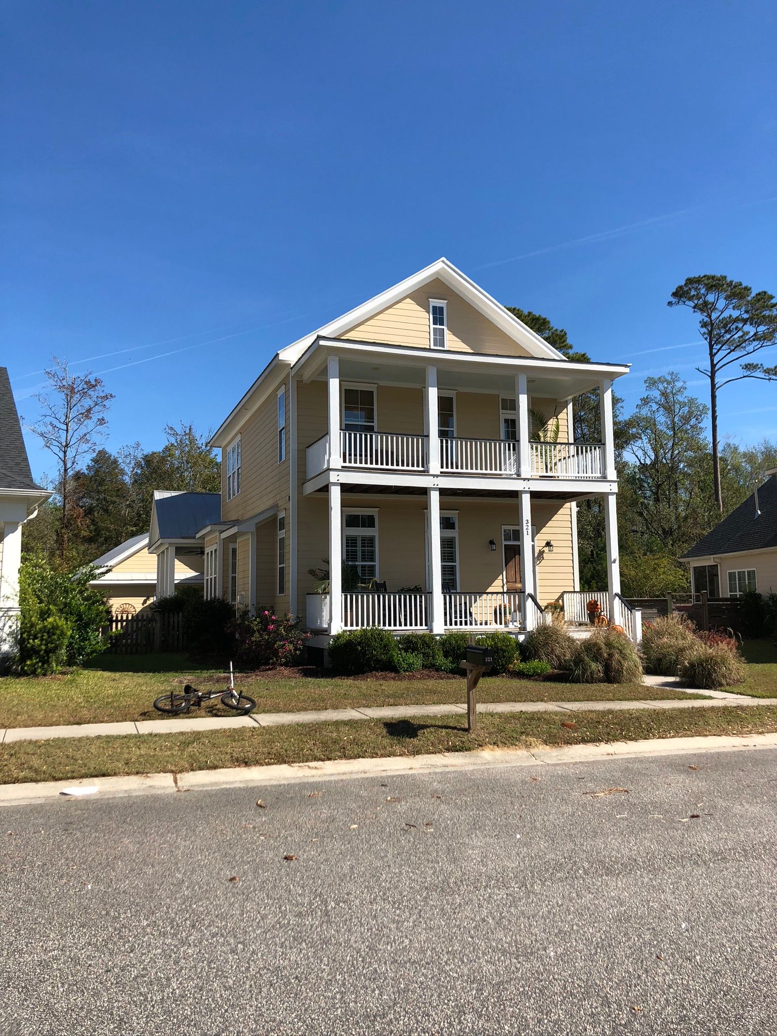 Two-story beige house with a porch and black railing against a clear blue sky.
