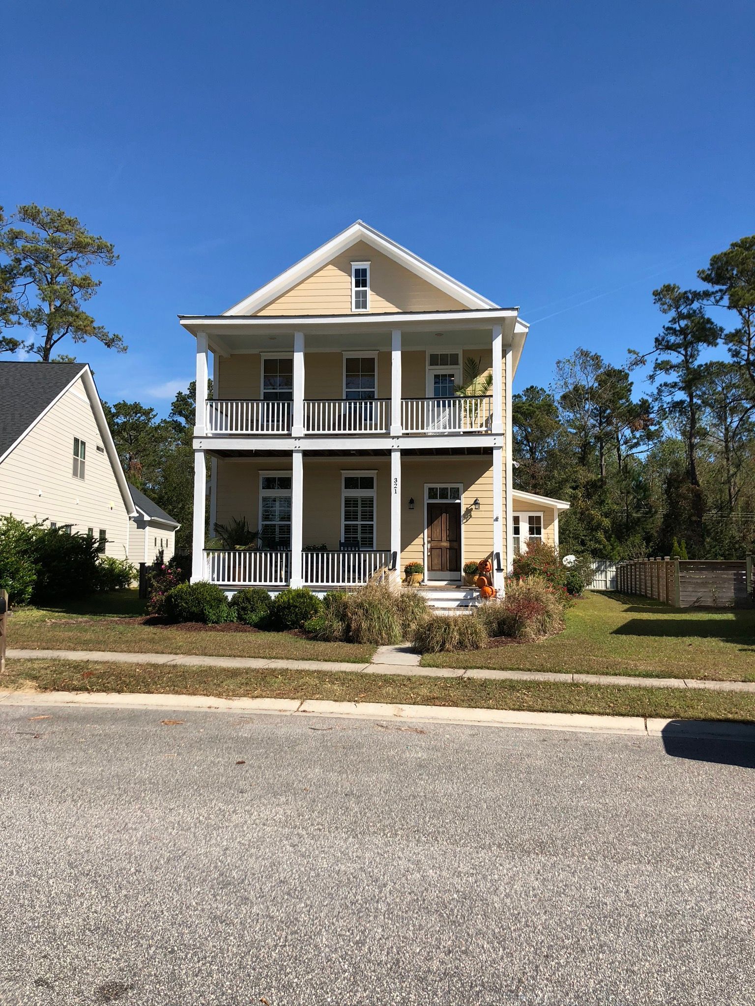 Two-story yellow house with white balconies, door, and trim; blue sky background.