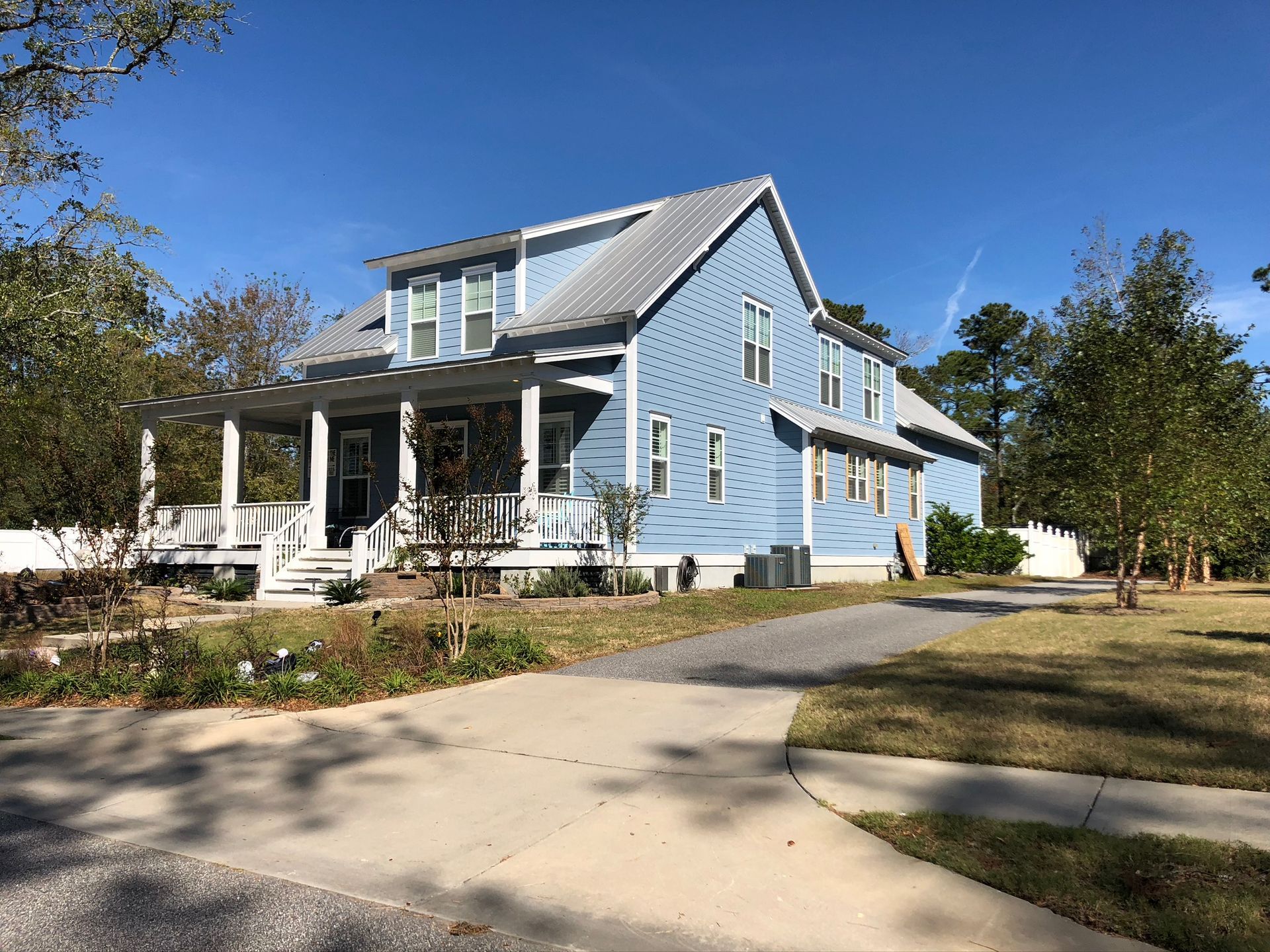 Blue two-story house with a porch and driveway on a sunny day.