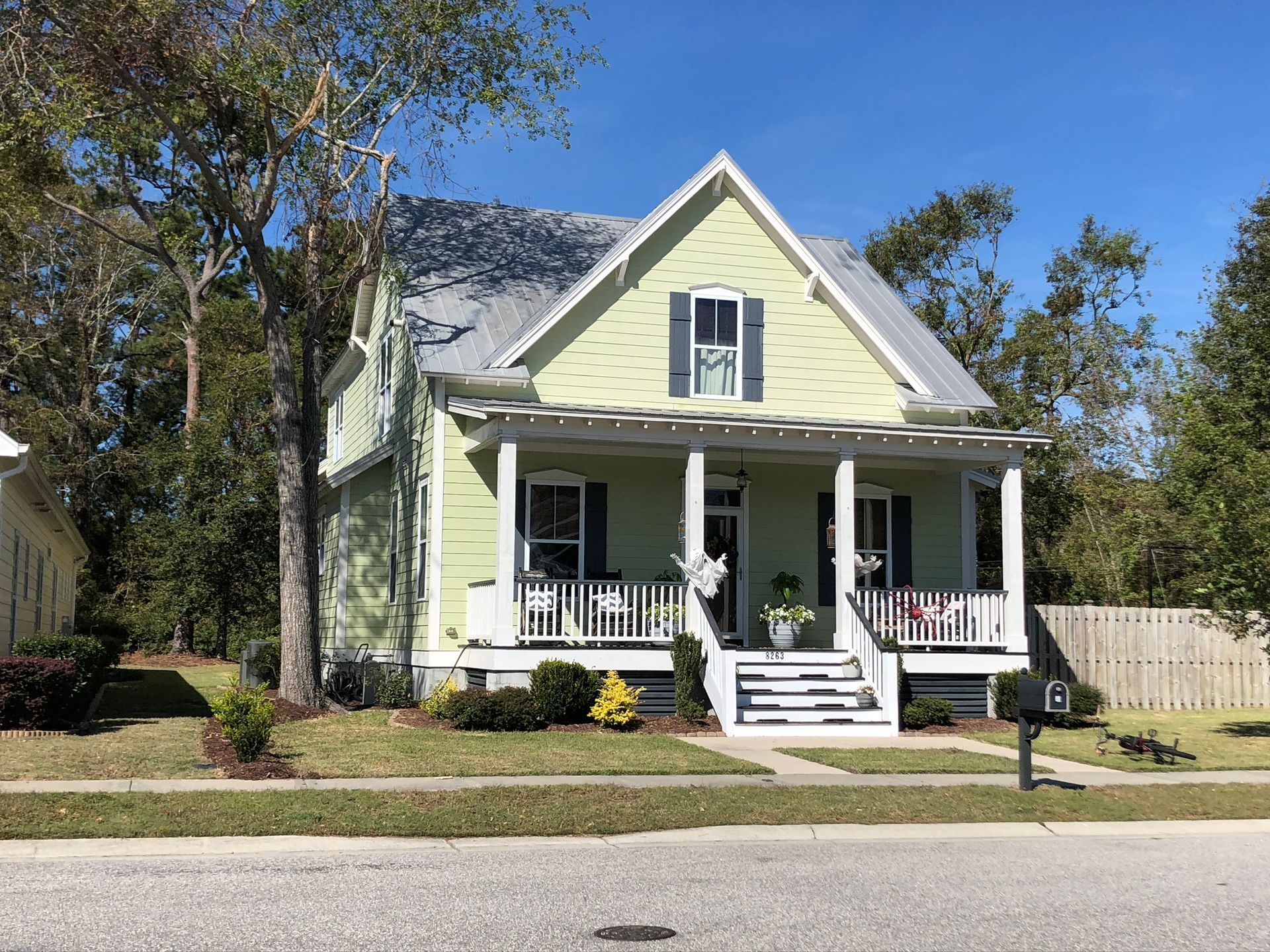 Green house with white porch, gray roof, and blue shutters on a sunny day.