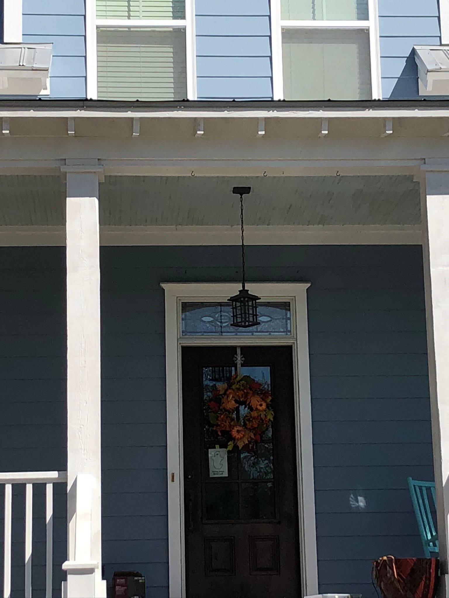 Blue house exterior with front door and fall wreath; porch with white columns; hanging lantern.