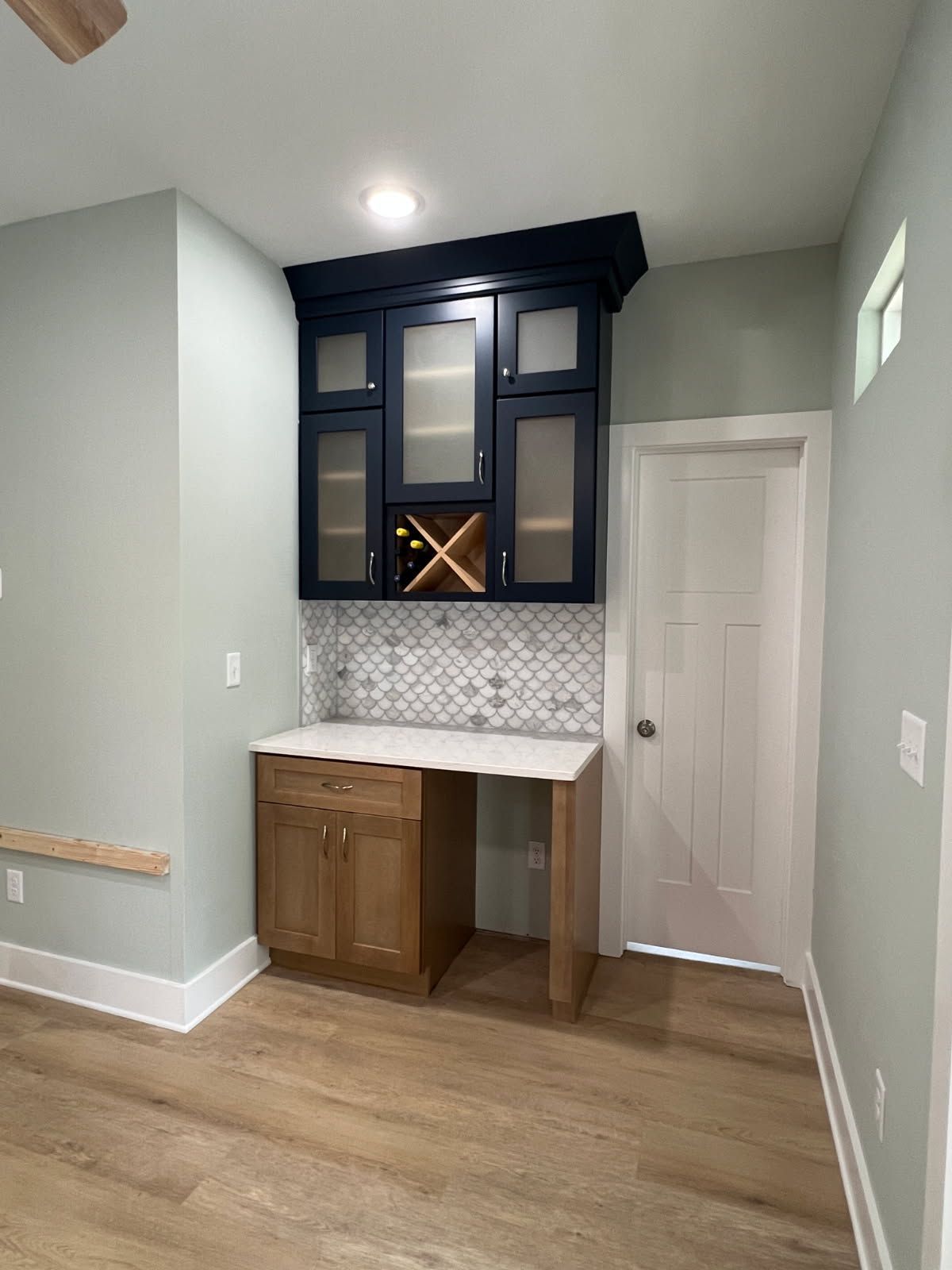 Built-in wet bar with dark blue upper cabinets, light wood lower cabinets, and a white countertop.