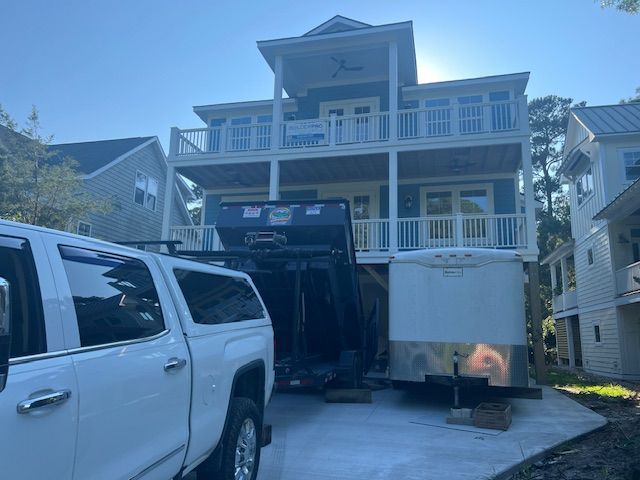 White pickup truck and trailer in front of a blue and white multi-story house.