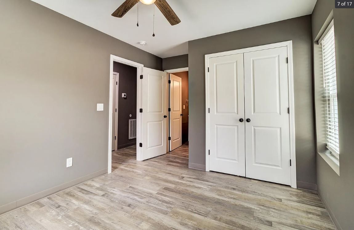 Bedroom with gray walls, white closet doors, wood-look floor, and ceiling fan.