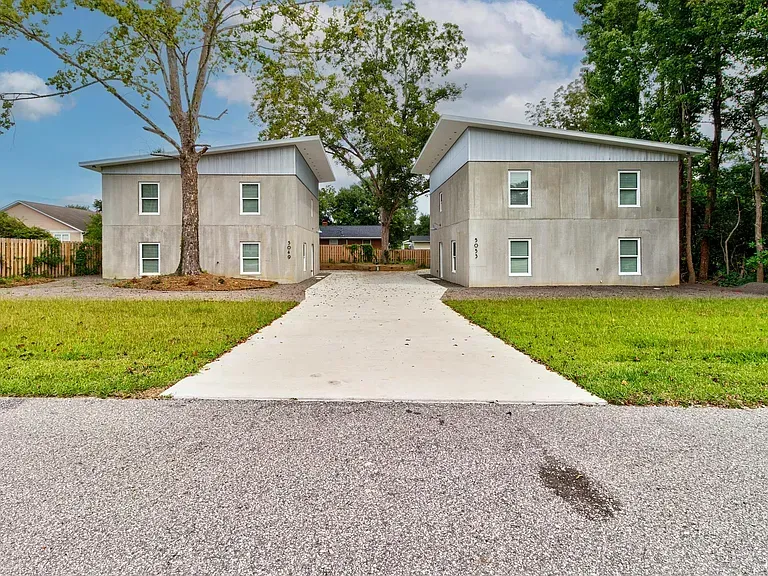 Two matching modern gray buildings with a shared concrete driveway. Green grass surrounds.