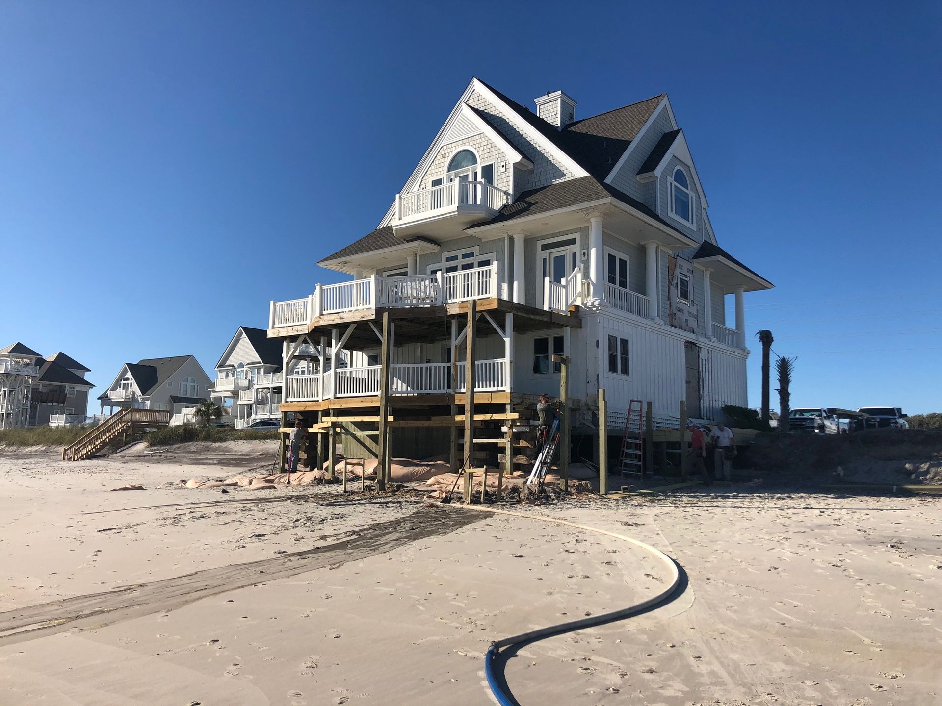 A large white house is sitting on top of a sandy beach.