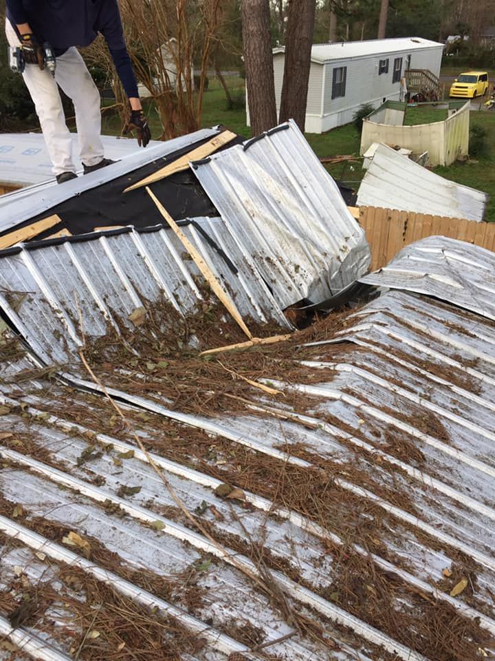 A man is standing on top of a roof that has been damaged by a storm.