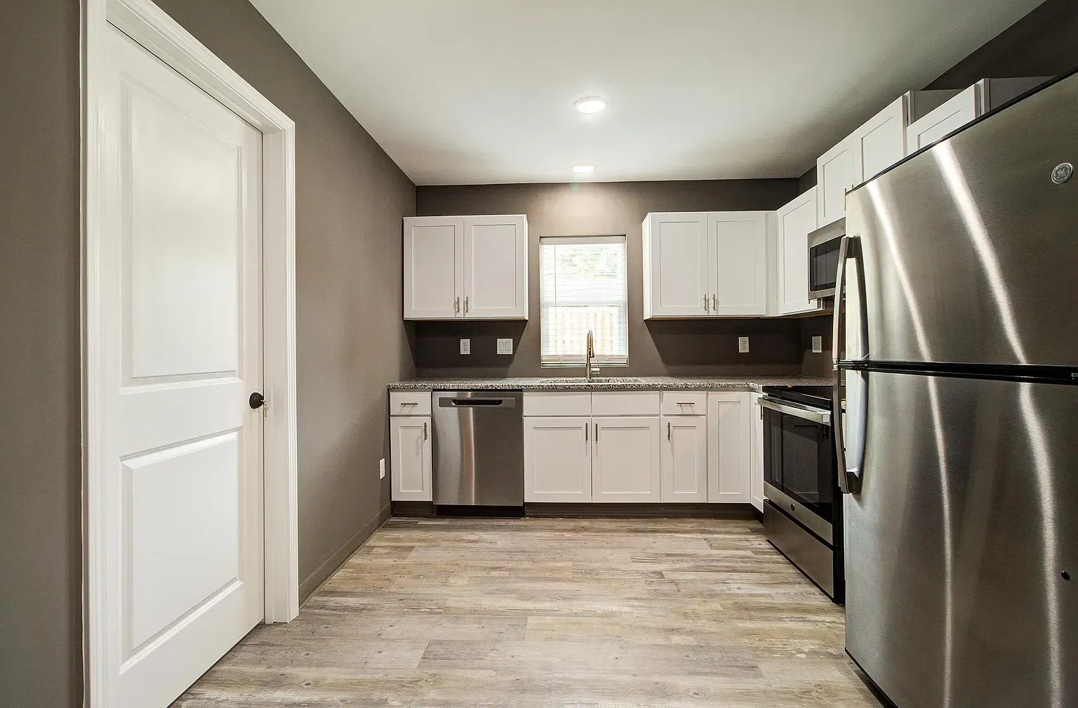 Modern kitchen with white cabinets, stainless steel appliances, gray walls, and light wood-look flooring.
