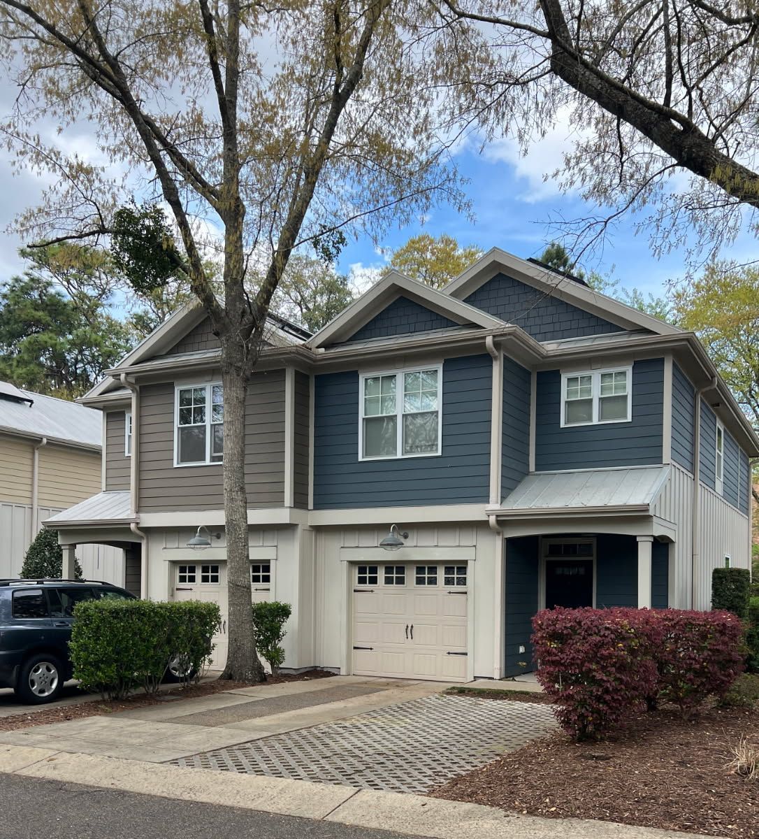 Two-story townhouses with beige and blue siding, white trim, and attached garages. A tree shades the front.