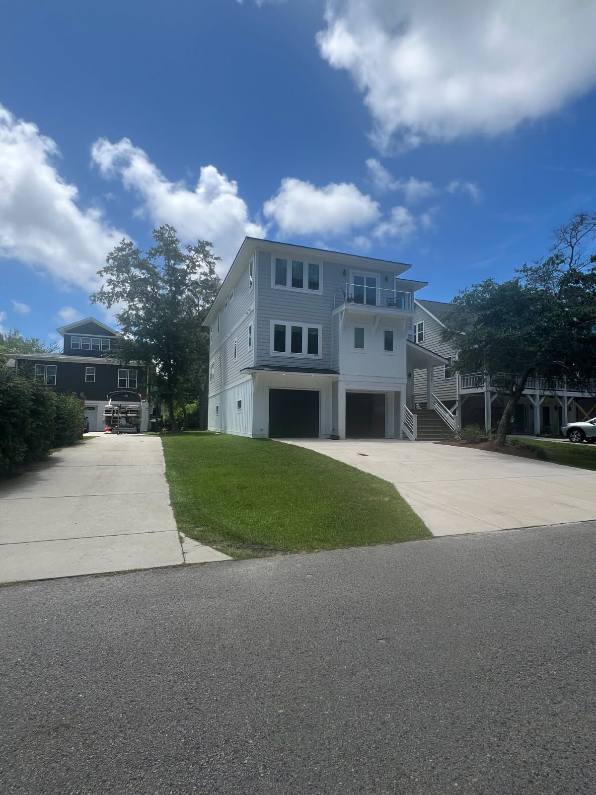 Three-story light blue house with two garages and white accents under a blue sky.