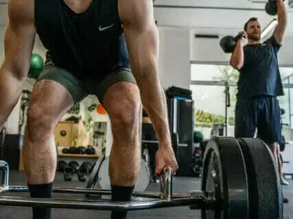 A man is squatting down to lift a barbell in a gym.