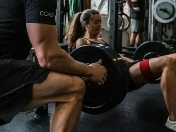 A man is helping a woman squat with a barbell in a gym