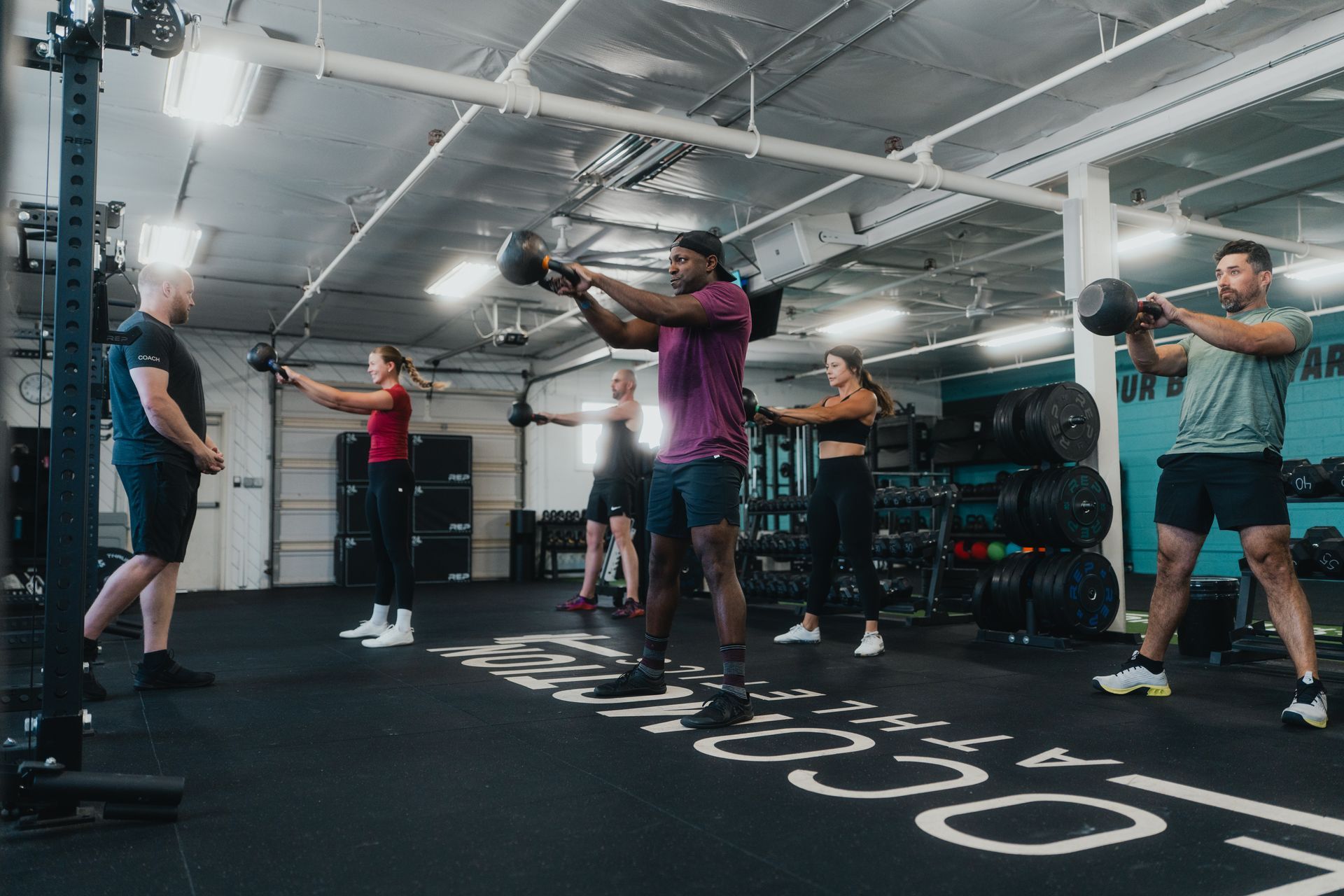 A group of people are doing kettlebell exercises in a gym.