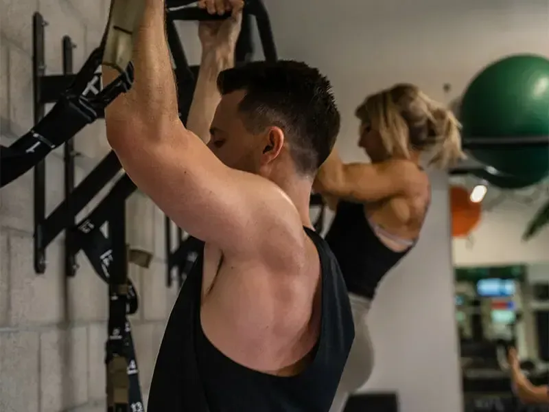 A man and a woman are doing pull ups in a gym.