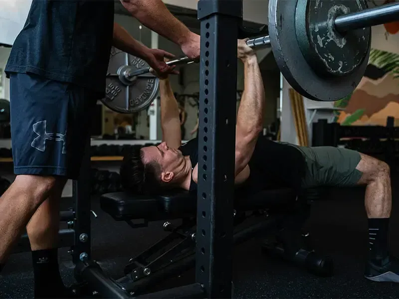 A man is lifting a barbell on a bench in a gym.