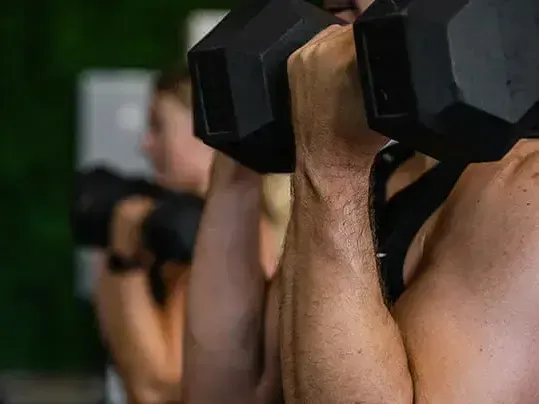 A man and a woman are lifting dumbbells in a gym.