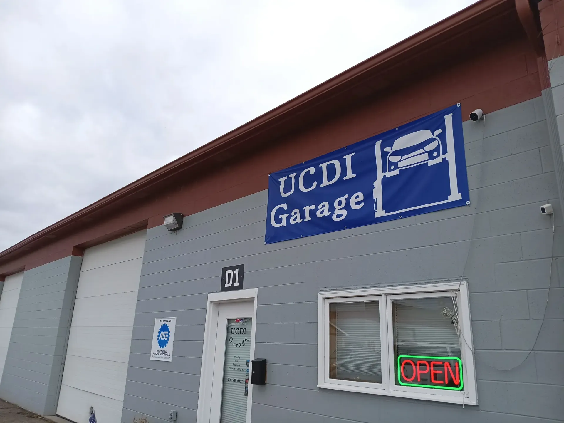 UCDI Garage exterior with blue sign and a red “OPEN” neon sign by the door