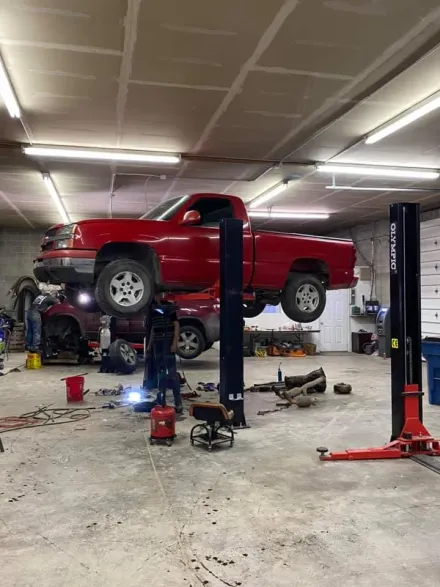 Red pickup truck raised on a lift in an auto repair shop with tools and equipment nearby