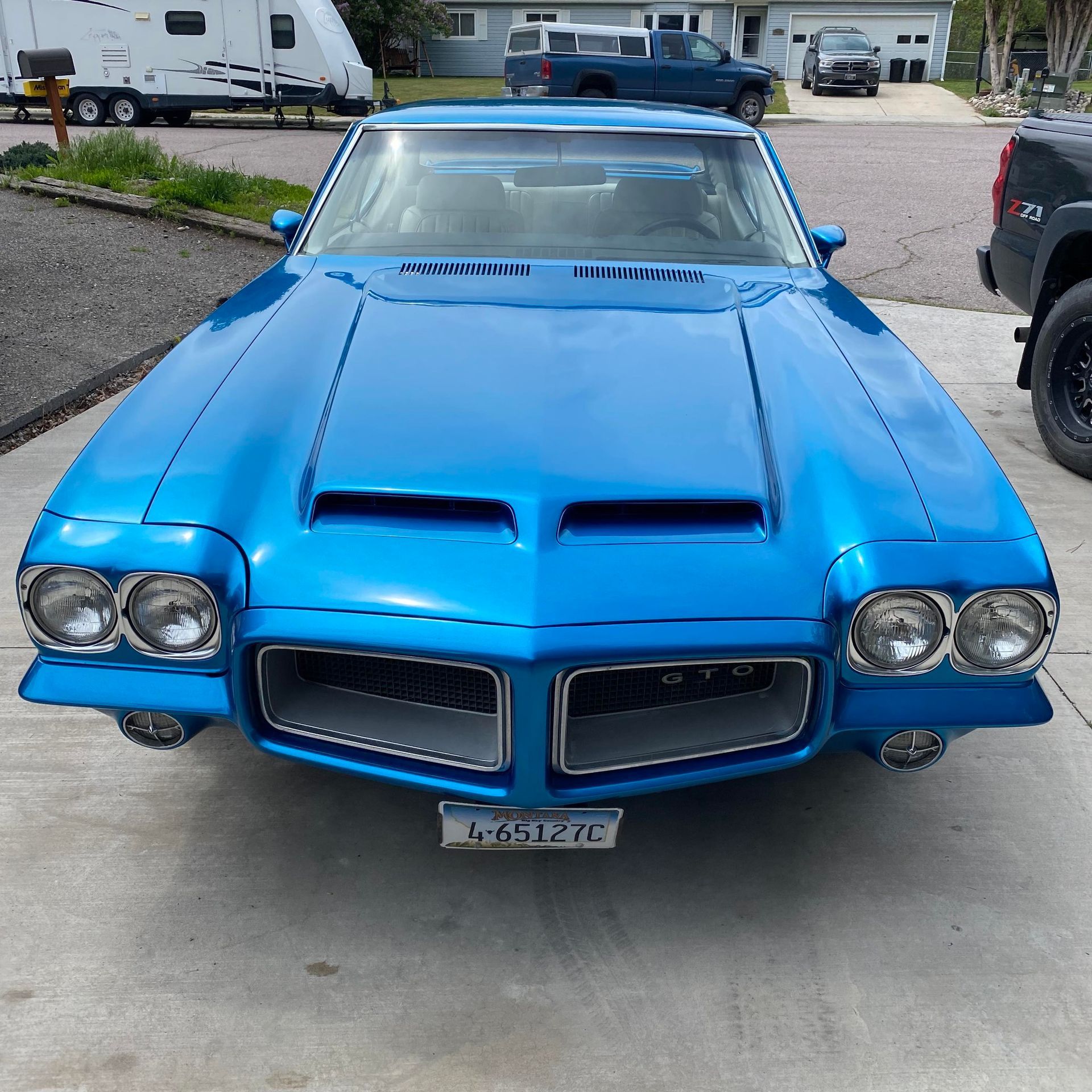 Bright blue classic Pontiac car parked on a driveway, front view with twin hood scoops and quad headlights
