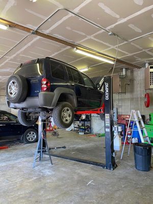 Black SUV lifted on a garage hoist inside an auto repair shop, with tools and equipment nearby.