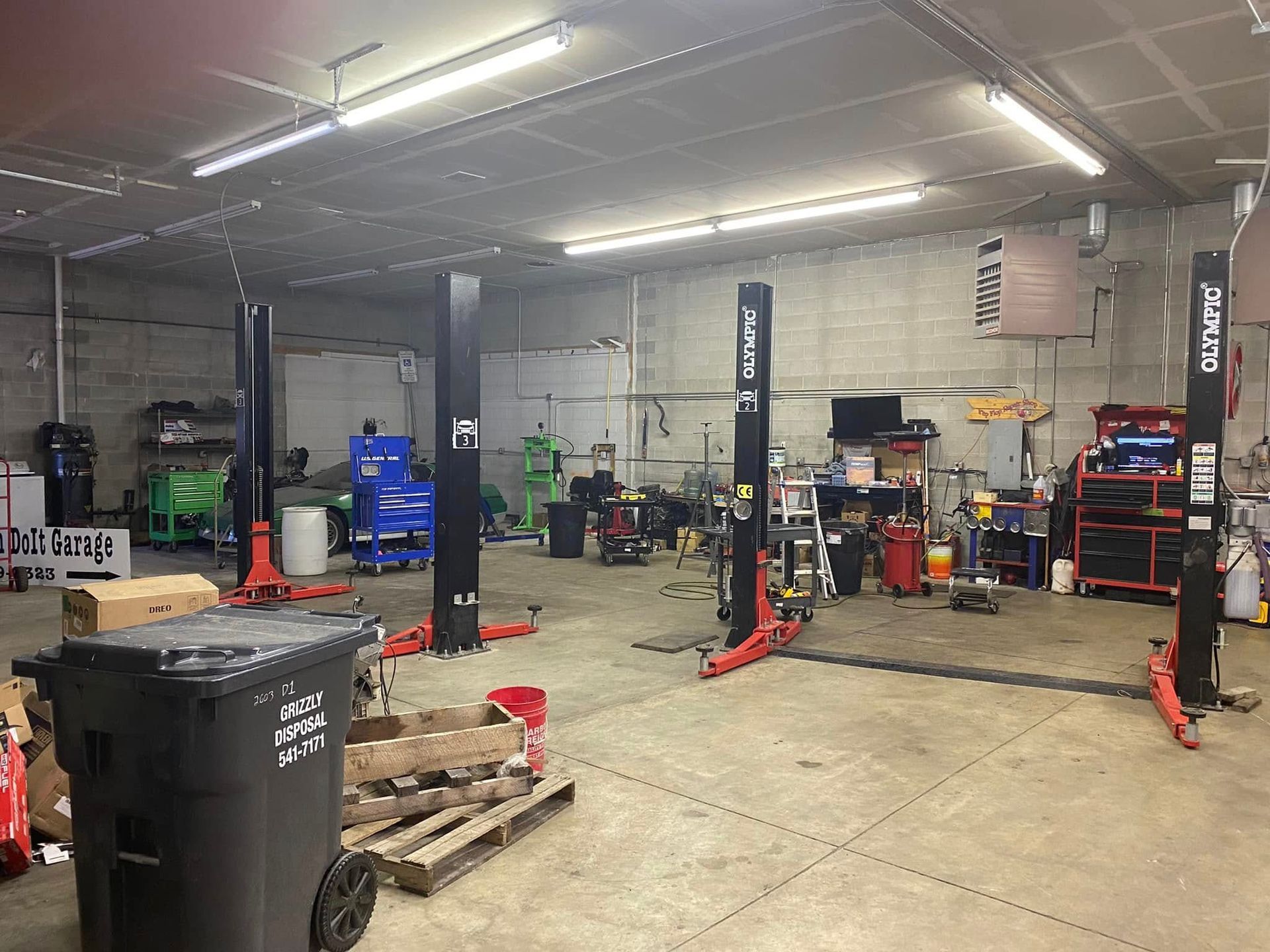 Auto repair shop interior with lifts, tools, parts, and a trash bin on a concrete floor