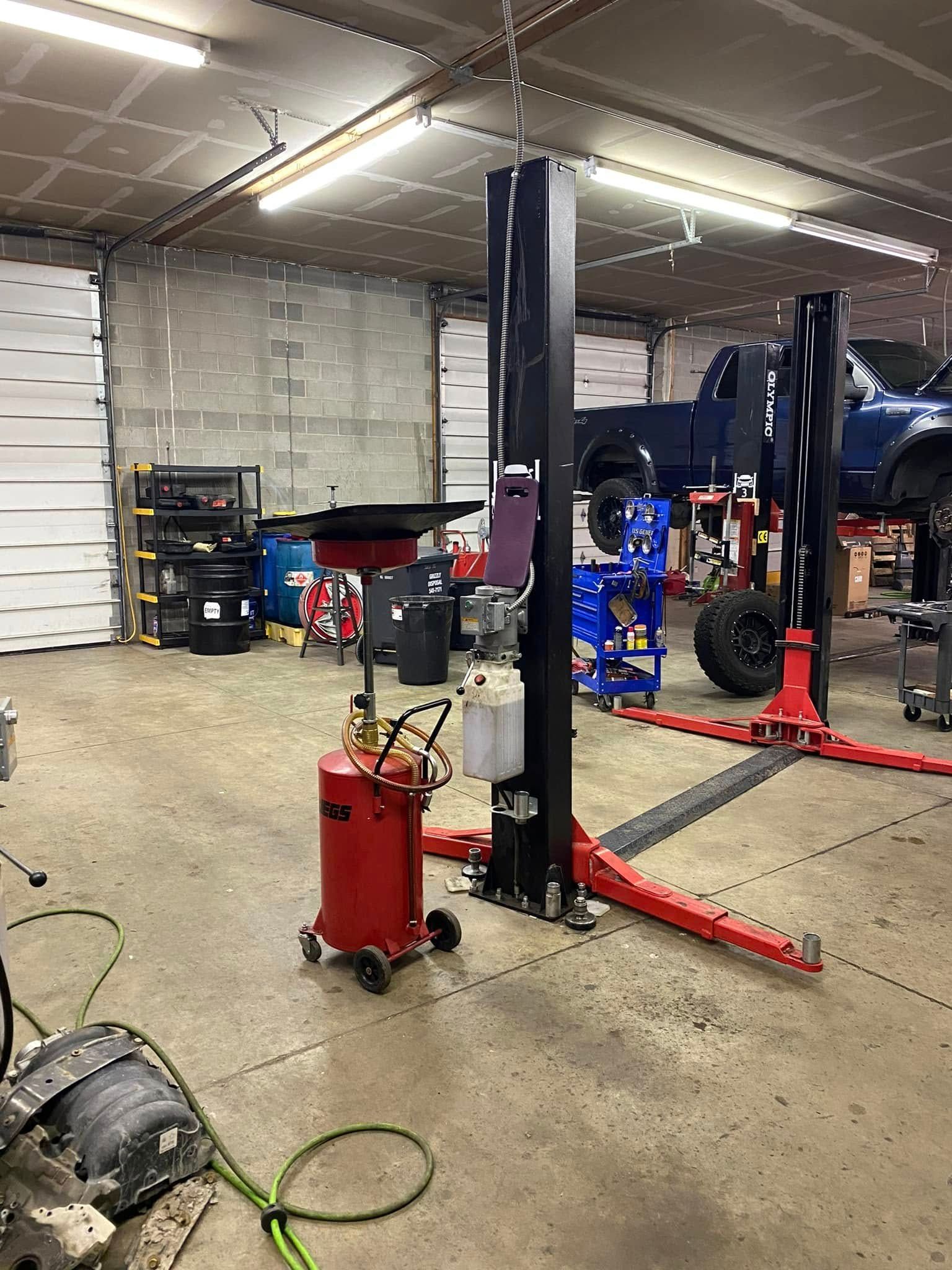 Auto repair shop with car lifts, tools, and a red rolling air compressor on the floor.