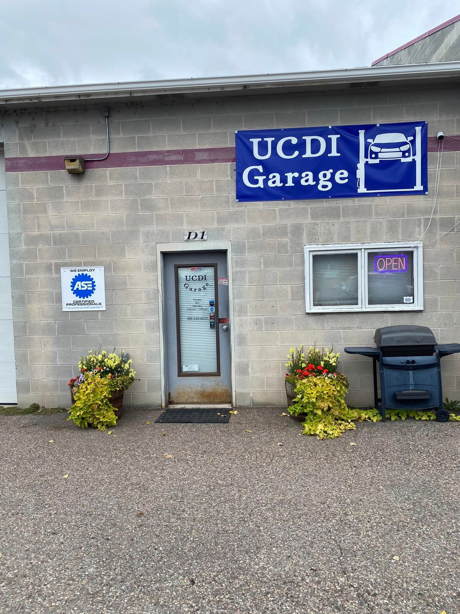 UCDI Garage storefront with blue sign, glass door, windows, potted plants, and trash bin