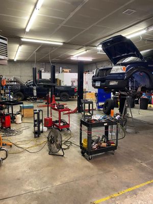 Auto repair shop with cars on lifts, tools, and equipment scattered across the garage floor.