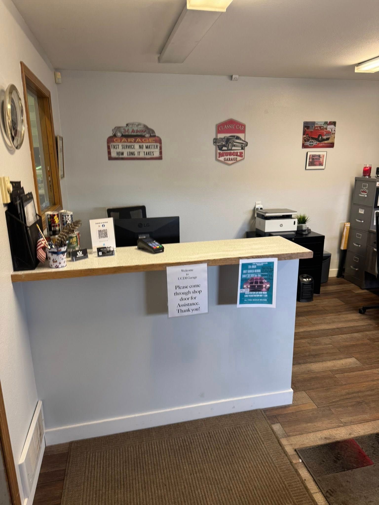 Small office reception desk with a computer, printer, wall signs, and a carpeted floor