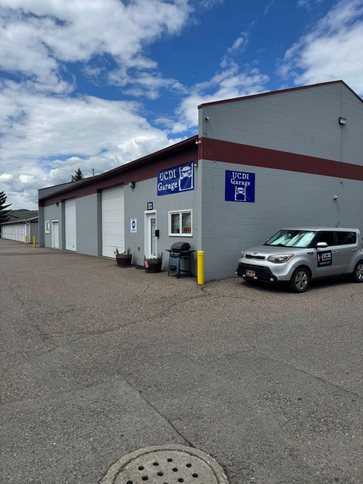 Warehouse exterior with blue signs and a parked silver SUV under a cloudy sky