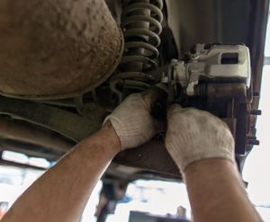 Gloved hands repairing a car’s brake assembly under the vehicle