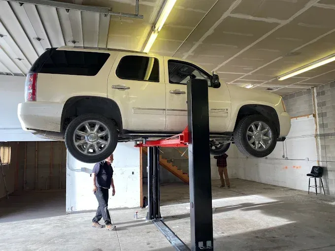 SUV lifted on a two-post car lift inside a garage, with two people working underneath.