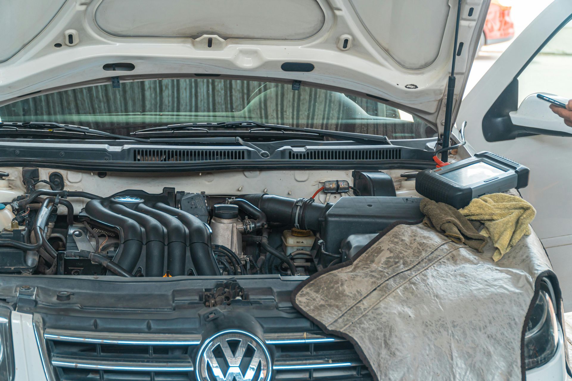 Open Volkswagen engine bay with hood raised and a cloth draped over the front grille