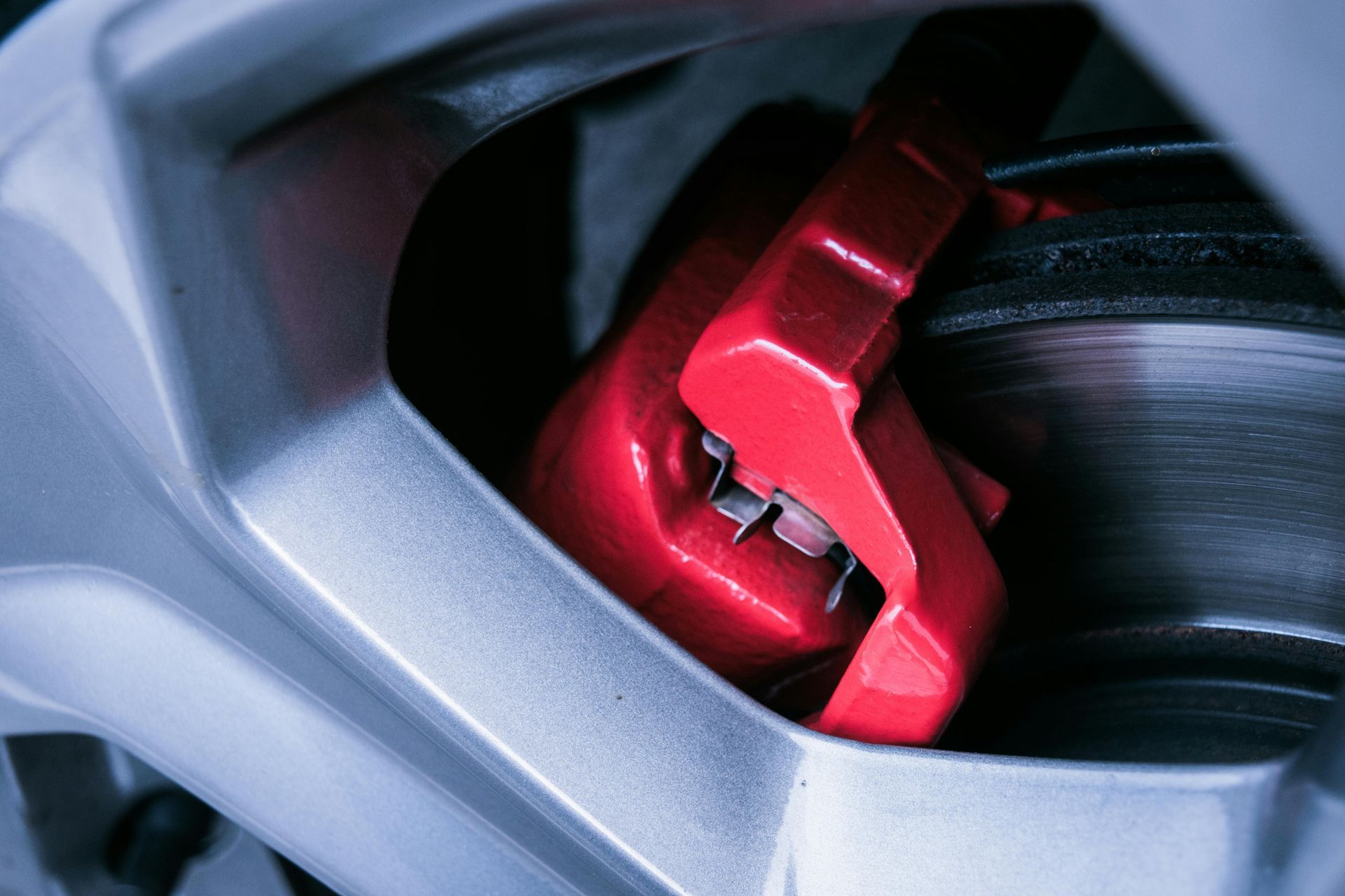 Red car brake caliper behind a silver wheel rim in close-up