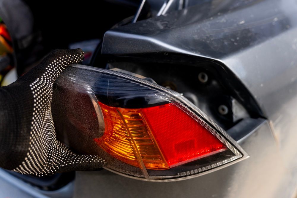 Hand gloved in mesh touching a car’s red and amber taillight close-up