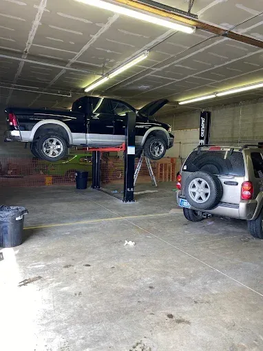 Two SUVs in a garage, one black vehicle raised on a lift with its hood open.