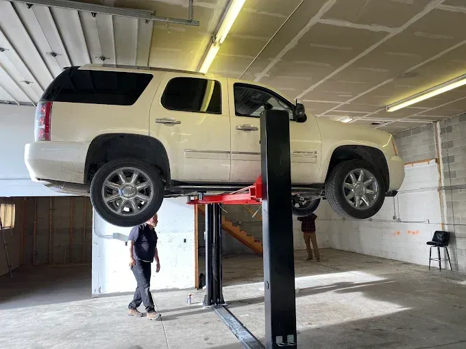 White SUV lifted on a two-post car lift inside a garage, with two people standing nearby