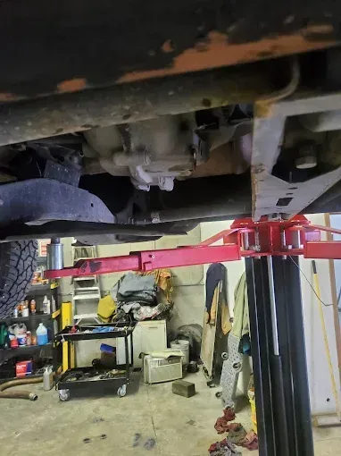 Under-car view of a vehicle on a red hydraulic lift in an auto repair garage