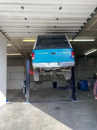 Blue SUV lifted on a car hoist inside a garage with its rear facing the camera