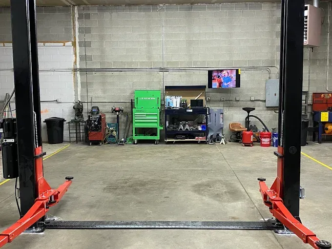 Empty auto shop bay with a car lift, concrete floor, and tools along the back wall.