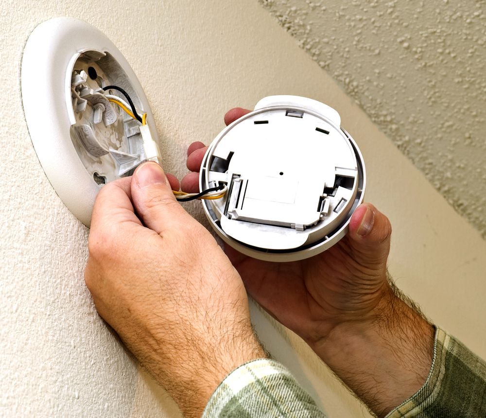 Hands Installing a Smoke Detector. Wires Connect to the Ceiling Mount — Powered By JBES In Sandgate, NSW