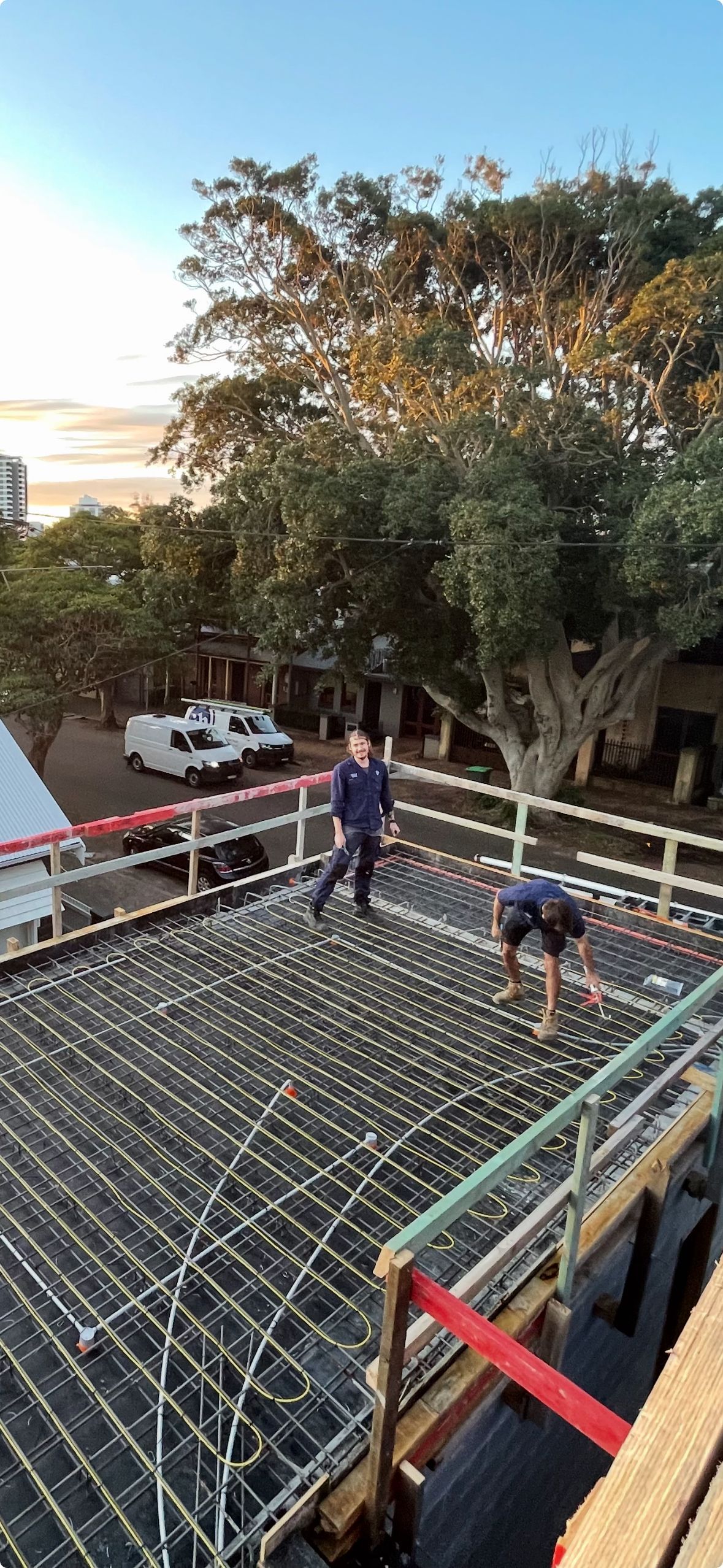 Two people on a rooftop with grid-like framework; trees and a van are in the background.Powered By JBES In Sandgate, NSW