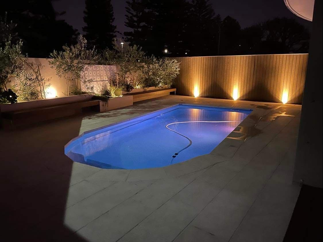Nighttime view of a backyard pool with surrounding lights and foliage.Powered By JBES In Sandgate, NSW