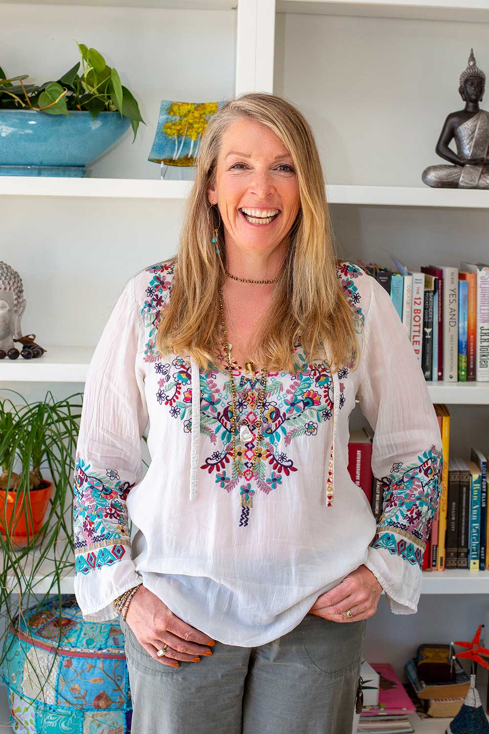 A woman is standing in front of a bookshelf with her hands on her hips.