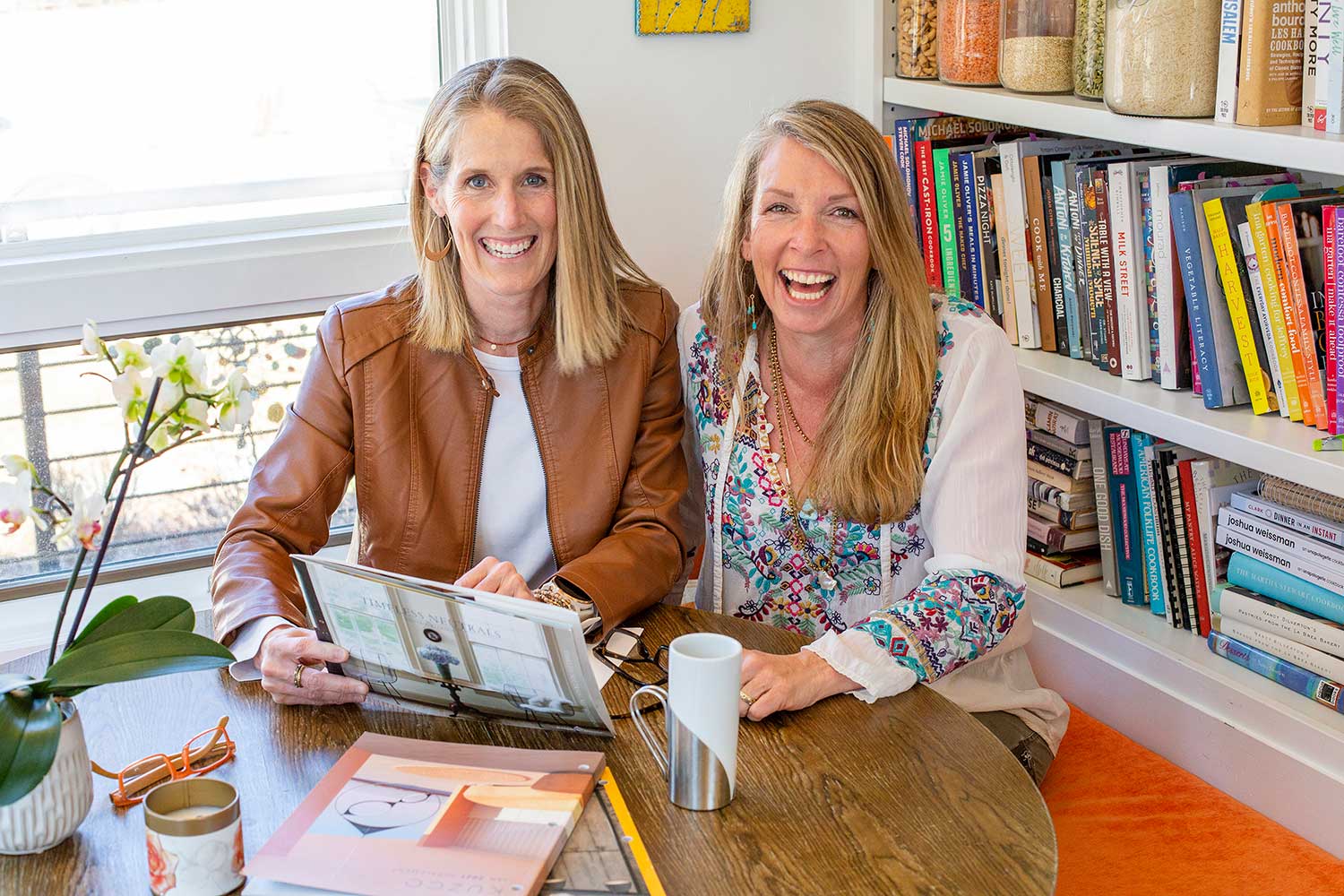 Two women are sitting at a table in front of a bookshelf.