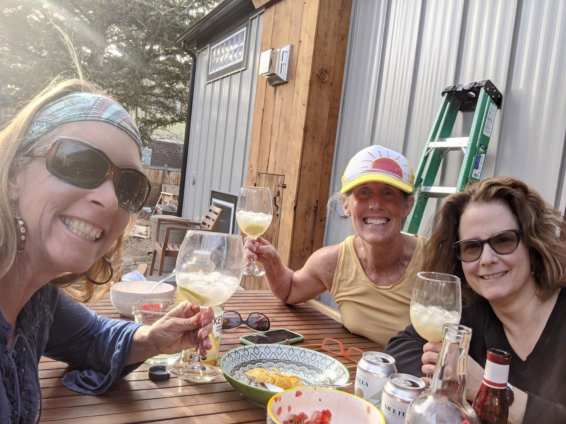 Three women are sitting at a table holding wine glasses and smiling.