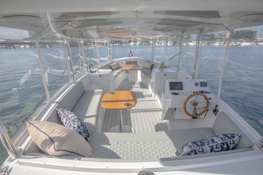 Interior of a boat with clear windows, seating, tables, and a steering wheel.