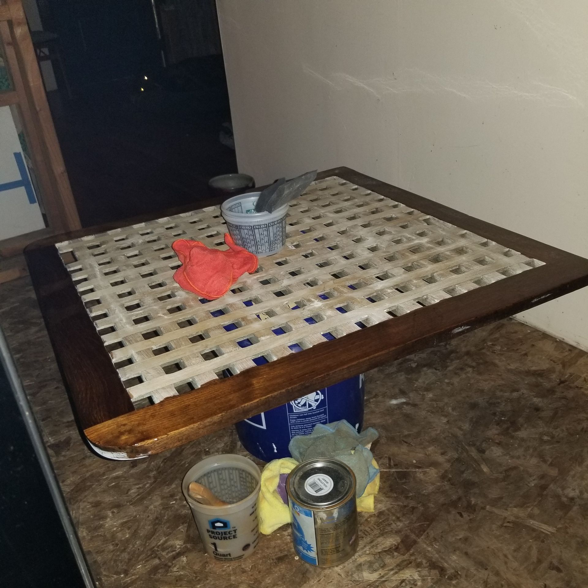 Wooden table with latticework top, supported by a bucket. Several objects rest on table surface.